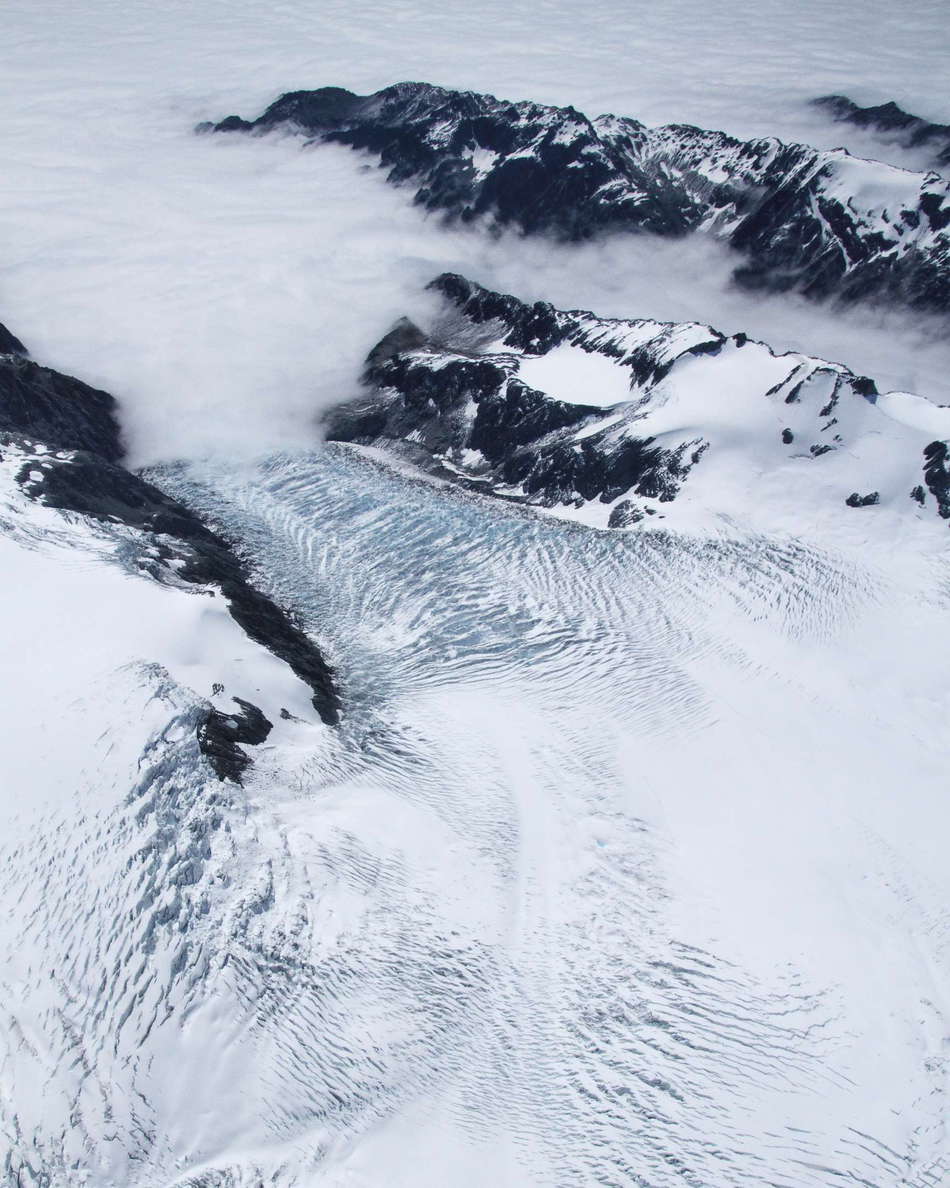 Location: Westland/Tai Poutini NP. Fully exposed to the cool and humid air brought by the prevailing westerly winds, the accumulation areas of the glaciers west of the divide receive a huge amount of snowfall. This results in low equilibrium lines and glacier tongues terminating close to the sea level, here disappearing under a dense layer of clouds. WI_nz478a.jpg