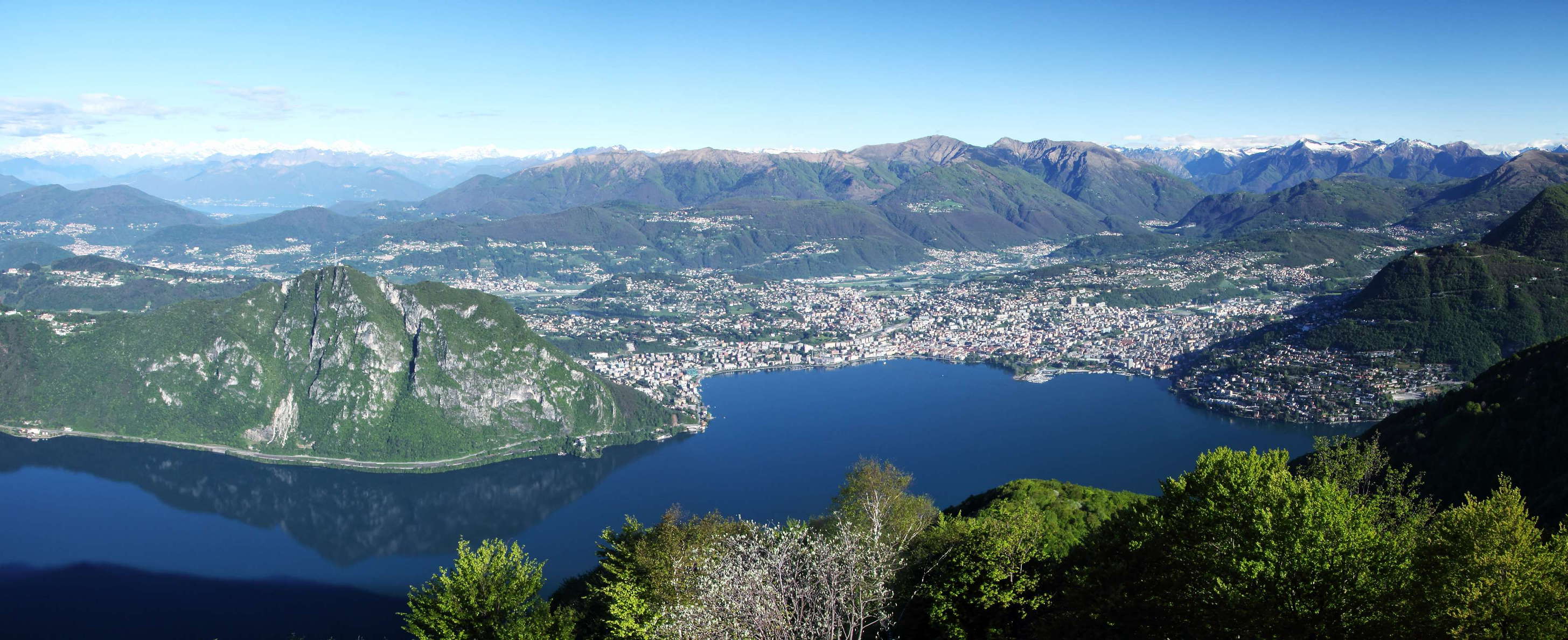 View from Sighignola. Left centre: Monte San Salvatore (912 m) reflecting in Lago di Lugano. Right centre: Lugano in front of Monte Tamaro (1962 m). In the left background, the Valais Alps with Monte Rosa (very left, Dufourspitze, 4634 m) and Dom (4545 m) are visible at a distance of 85 km. WI_ch112c.jpg