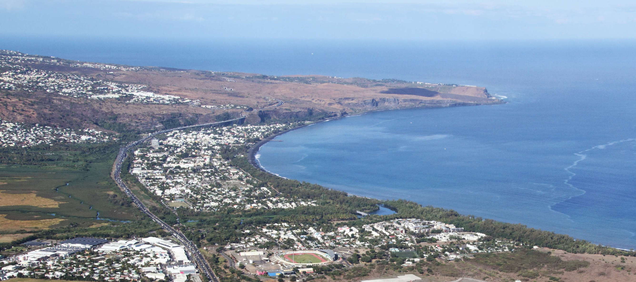 View towards southwest. Saint-Paul is seen in the foreground and centre of the image, the peninsula of the Cap de la Houssaye with its savanna landscape appears behind. The motorway running through the scene is the Route des Tamarins, part of the connection between Saint-Denis and Saint-Pierre. WI_re040.jpg